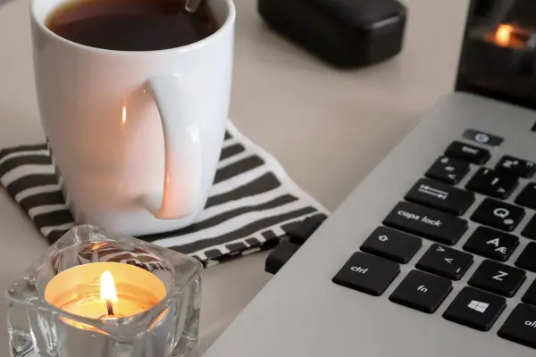 Schreibtisch au f dem ein Laptop, Kaffee und eine Kerze stehen